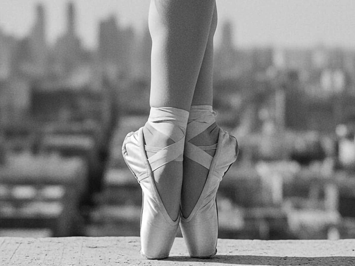 Black-and-white image of a ballerina forming an arc with her arms, the negative space around her creating a cinematic…