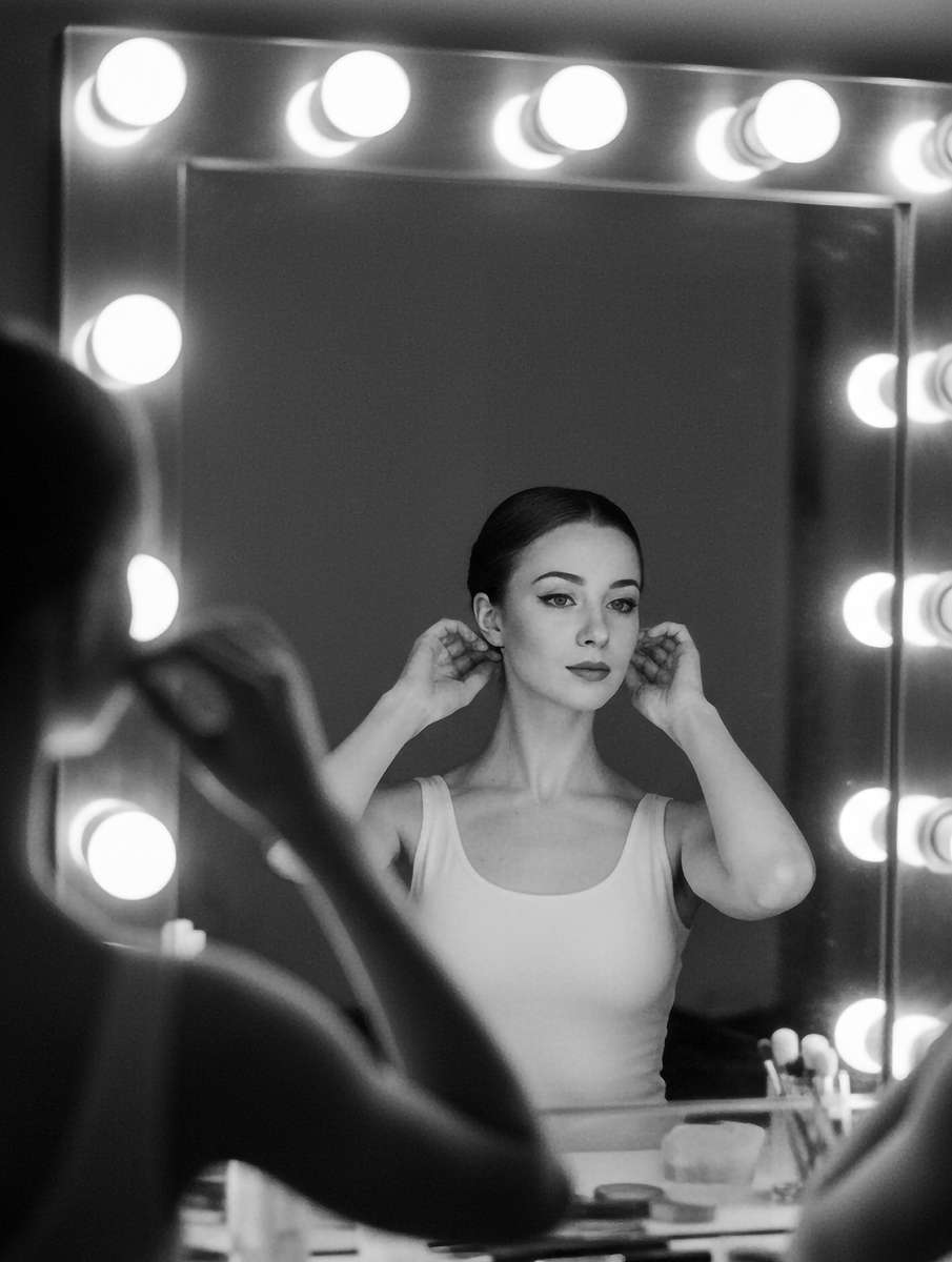 Backlit ballerina facing a mirror, silhouette and reflected features creating a dramatic narrative