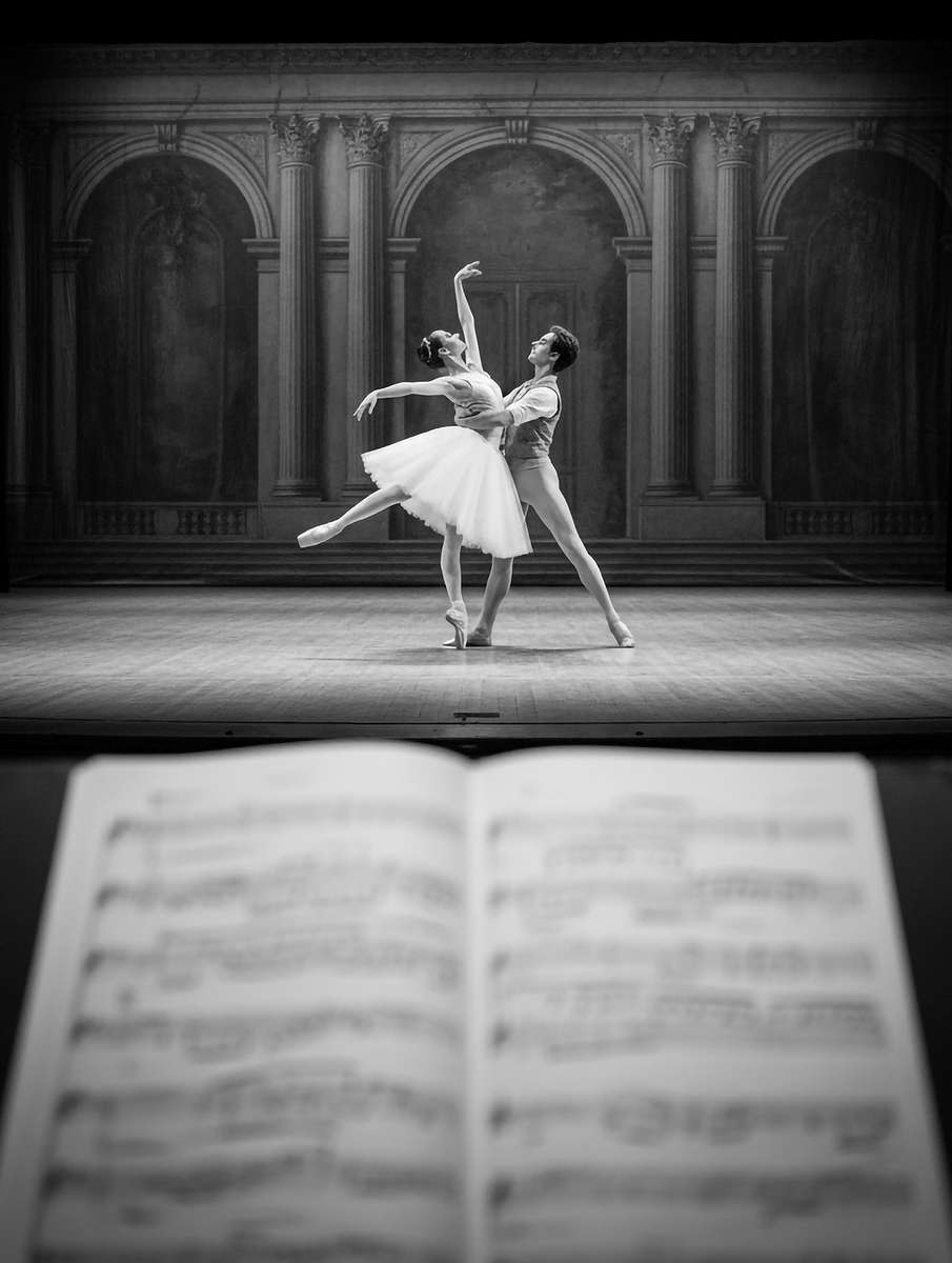 Ballet dancer captured mid first step with an extended arm and lifted chin, light tracing the line of the body