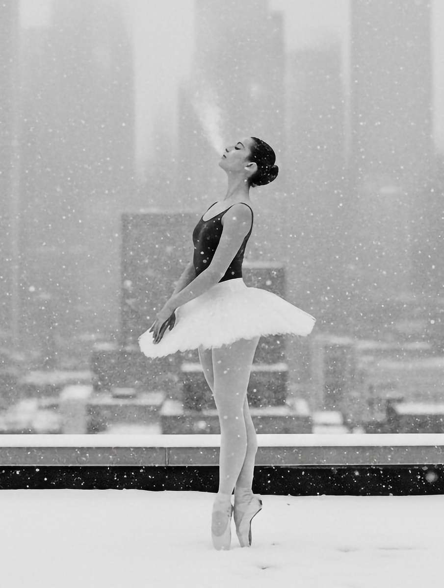 Two dancers performing a lift beneath a pale, overcast sky with snow gently falling