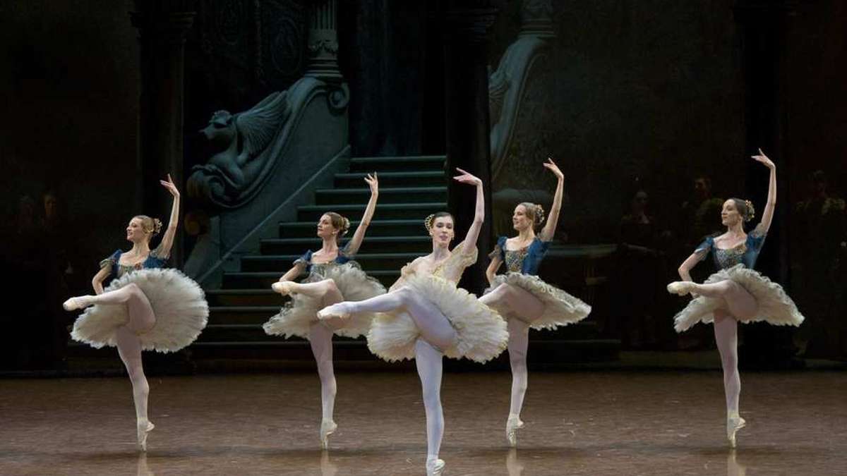 Stage scene of Paquita with warm Iberian colors contrasting against a pale chorus in white gala tunics