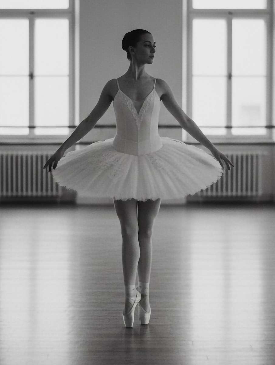Profile of a dancer mid-pose with soft lighting highlighting the controlled extension of her arm and the tension in her hands