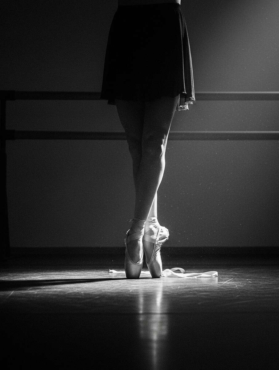 Ballerina extending into a long tendu with visible muscle definition and purposeful reach under studio lighting